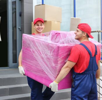 Umzug in Königstein Zwei Umzugshelfer tragen ein in Folie gepacktes Möbelstück – Umzug in Königstein