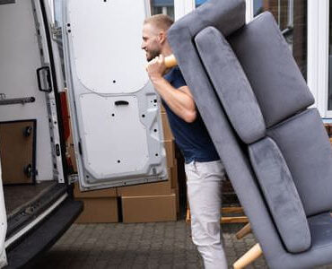 Möbellift Königstein Möbellift Königstein: Helfer tragen ein graues Sofa aus einem Transporter
